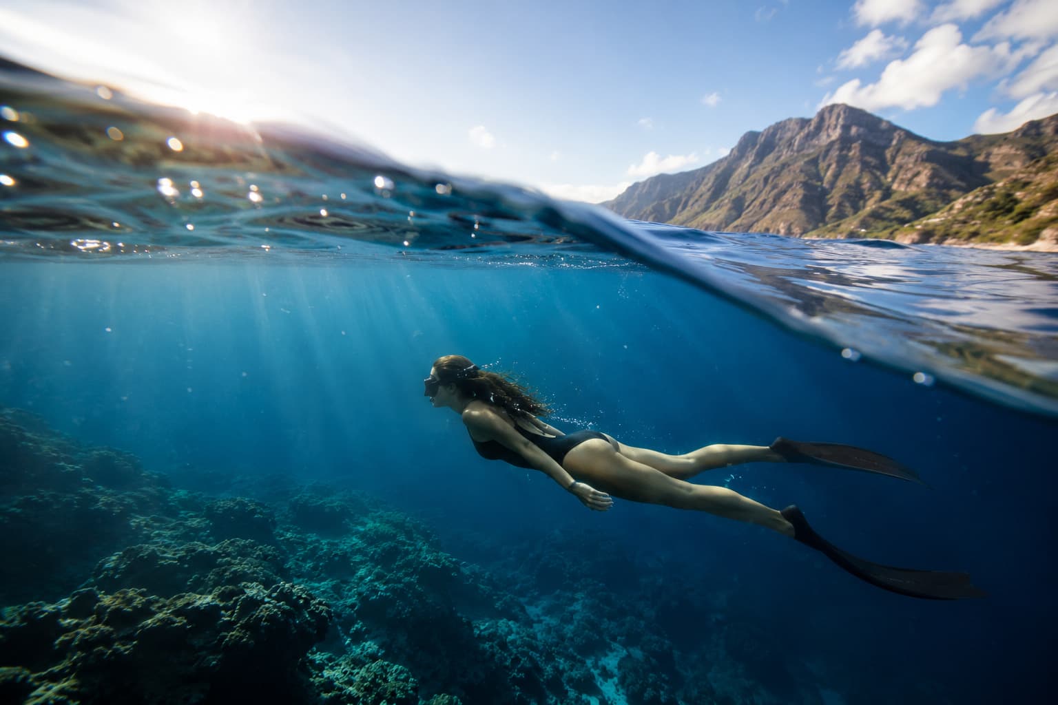 A freediver below the surface near a mountainous coastline